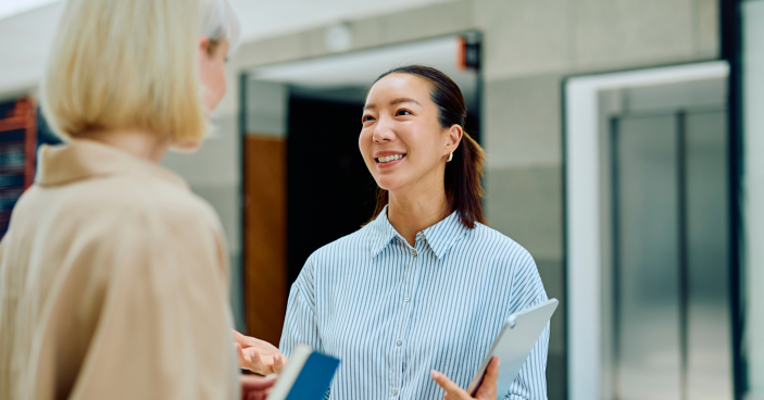 Smiling businesswomen communicating in modern office hallway